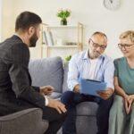 Mature couple reviewing paperwork on a clipboard with an agent during an in-home consultation