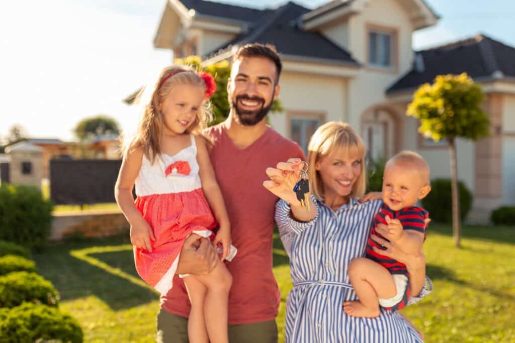 Close and Move Into Your New Home Smiling family of four holding house keys in front of their new home.