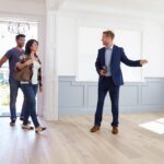 Real estate agent showing a couple around an empty home with wood flooring.