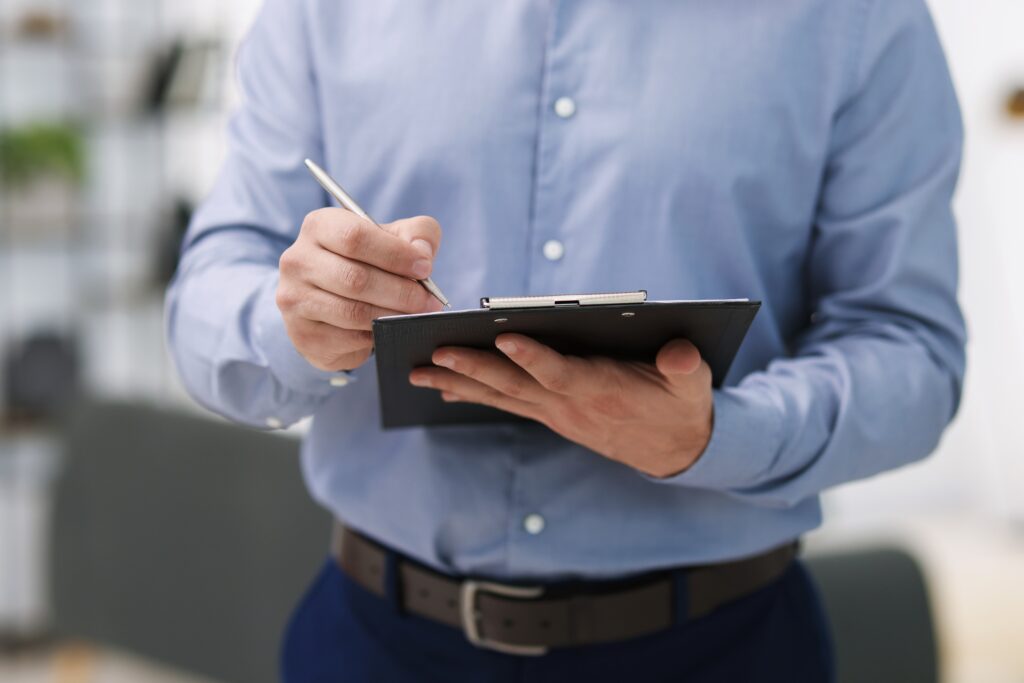Reviewing and Signing Home Buying Paperwork A professional in a blue shirt reviewing and signing paperwork on a clipboard